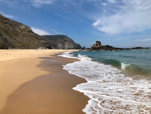 A beach with clear waters, a sandy shore, and rocky formations in the background.