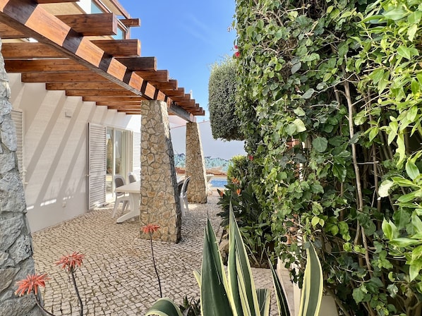 A stone pillar, a wooden pergola, and a tiled patio area with plants.