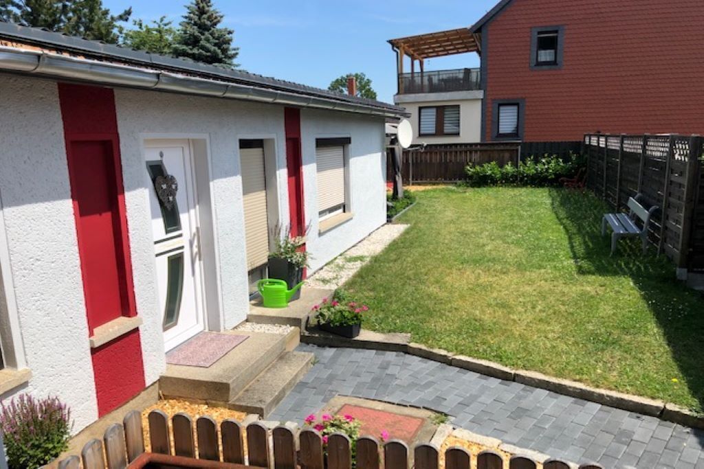 Una propiedad residencial con entrada pavimentada, un pequeño jardín y valla de madera.