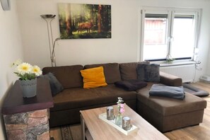 A living room with a brown sofa, a coffee table, and a painting of a forest scene.