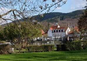 Un bâtiment historique avec un toit rouge, situé au bord d’un lac, avec un arbre au premier plan.