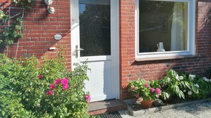 Ein rotes Backhaus mit weißer Tür und Fenster, einer kleinen Veranda und Blumentöpfen.