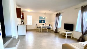 A spacious living area with a sofa, a TV, a dining table with chairs, and a kitchen area with cabinets and a refrigerator. - modern Apartment, only a few minutes to the beach and the city centre (Kvarner Bucht)