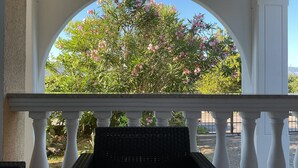 A covered outdoor area with a white balustrade, a wicker bench, and a view of a flowering tree. - modern Apartment, only a few minutes to the beach and the city centre (Kvarner Bucht)