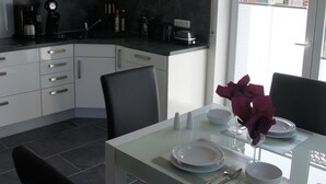 Una cuina moderna amb armaris blancs, una taula de dinar amb plats, una copa de vi i un ram de flors.