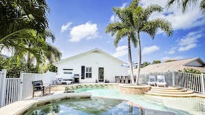 Una piscina con diseño de tablero de ajedrez, un edificio blanco con un letrero que dice 'Beach House', y palmeras.