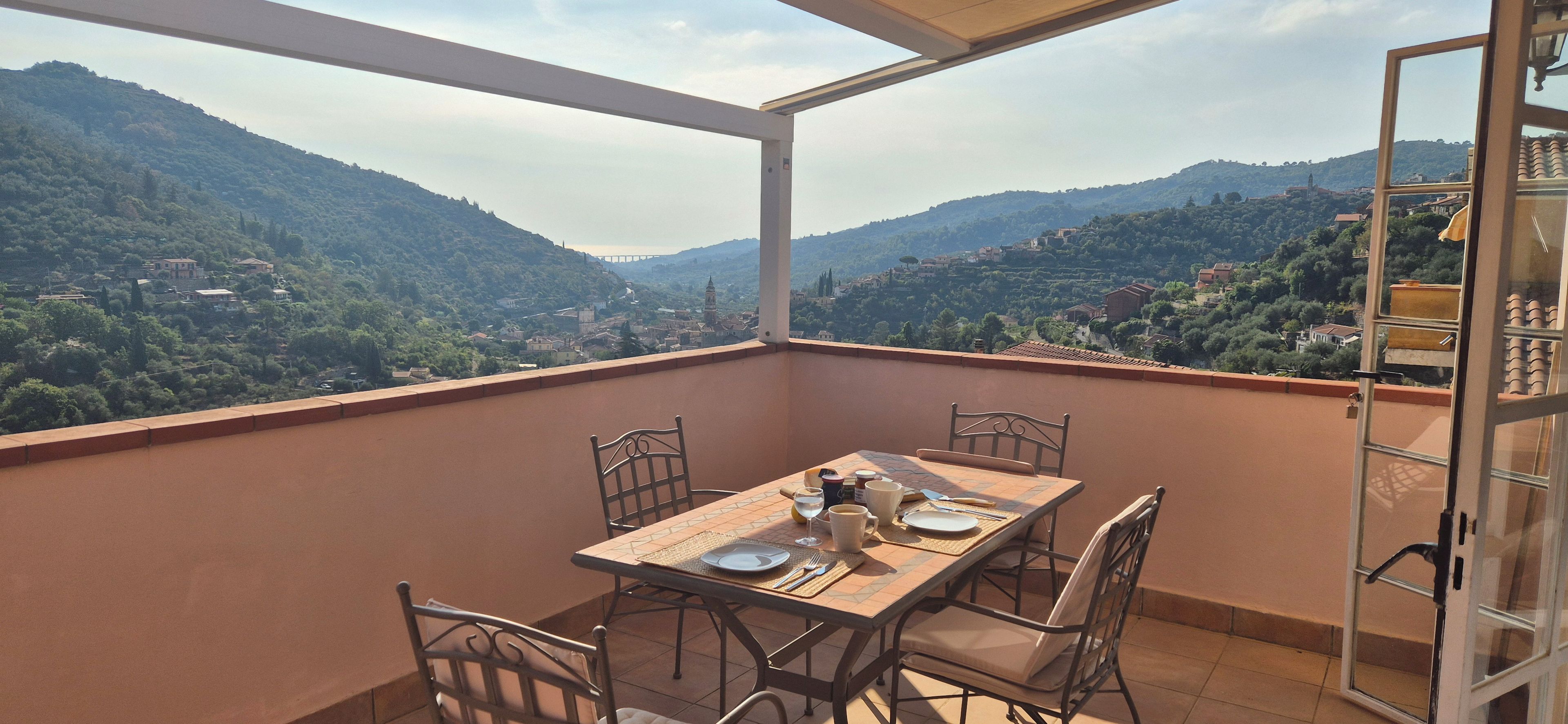 A balcony with a table set for two, overlooking a mountainous landscape.