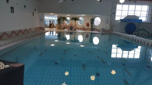 Una piscina interna con pavimento piastrellato, alcune sedie e un tavolo sullo sfondo.