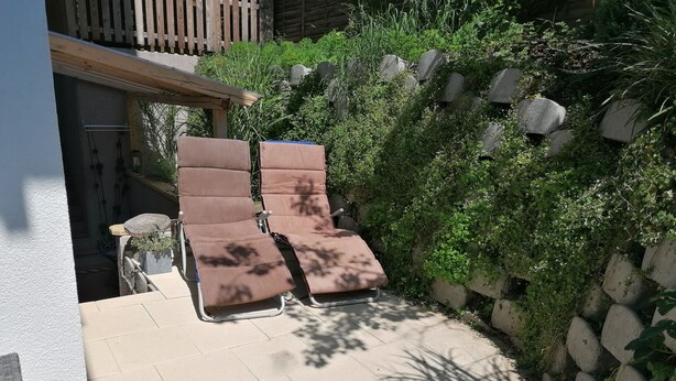 A patio with two sun loungers, a stone wall, and a wooden deck. - Apartment Auer family  (Tulfes)