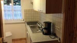 Una pequeña cocina con ventana, pileta, estufa y cafetera.