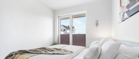 A bedroom with a bed, a window, and a view of houses.