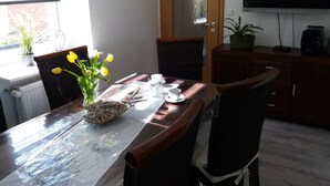 A dining area with a table set for two, a vase with yellow flowers, a newspaper, and a coffee maker.