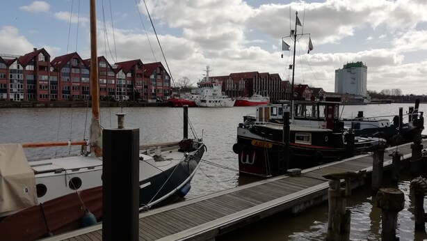 A dock with boats, a wooden pier, and buildings with red roofs in the background.