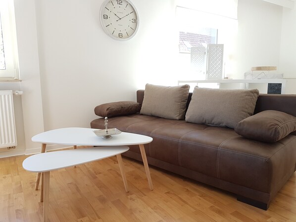 A modern living room with a brown leather sofa, a white coffee table, and a wall clock.