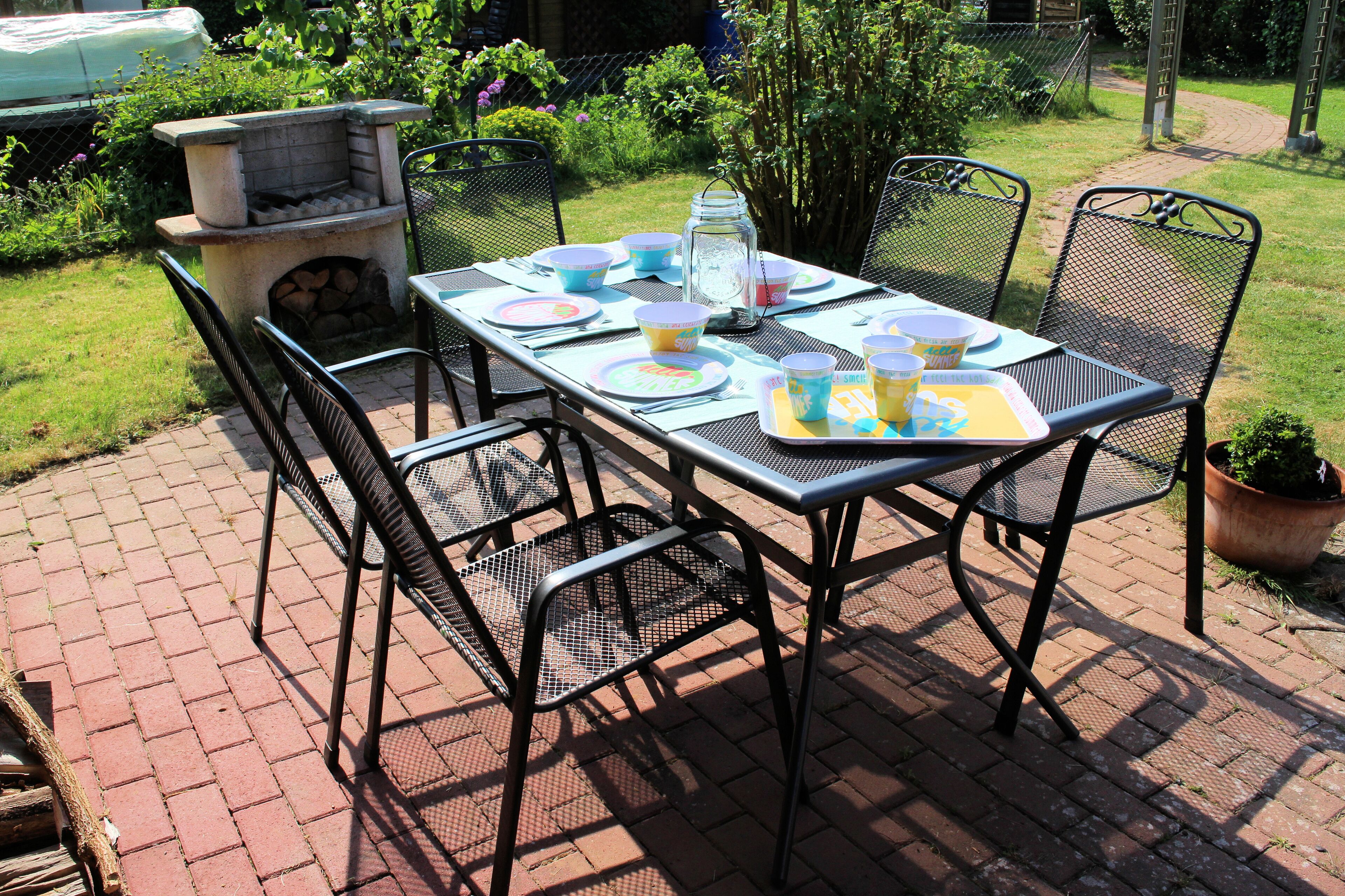 A patio table set with plates, cups, and a tray, surrounded by chairs.