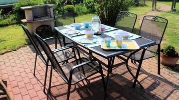 A patio table set with plates, cups, and a tray, surrounded by chairs.