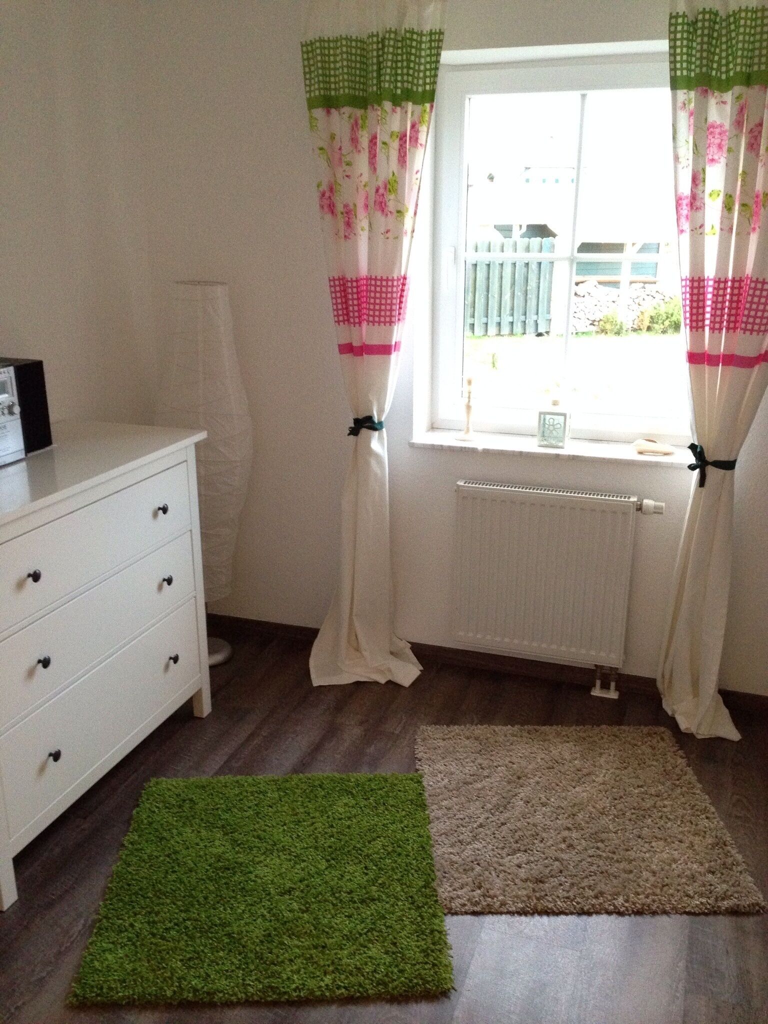 A room with a white dresser, a radiator, and two rugs, one green and one beige.