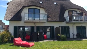 A two-story house with a thatched roof, a balcony, and a small garden with a red sofa.