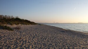 A beach with a clear sky and the sun setting over the water.