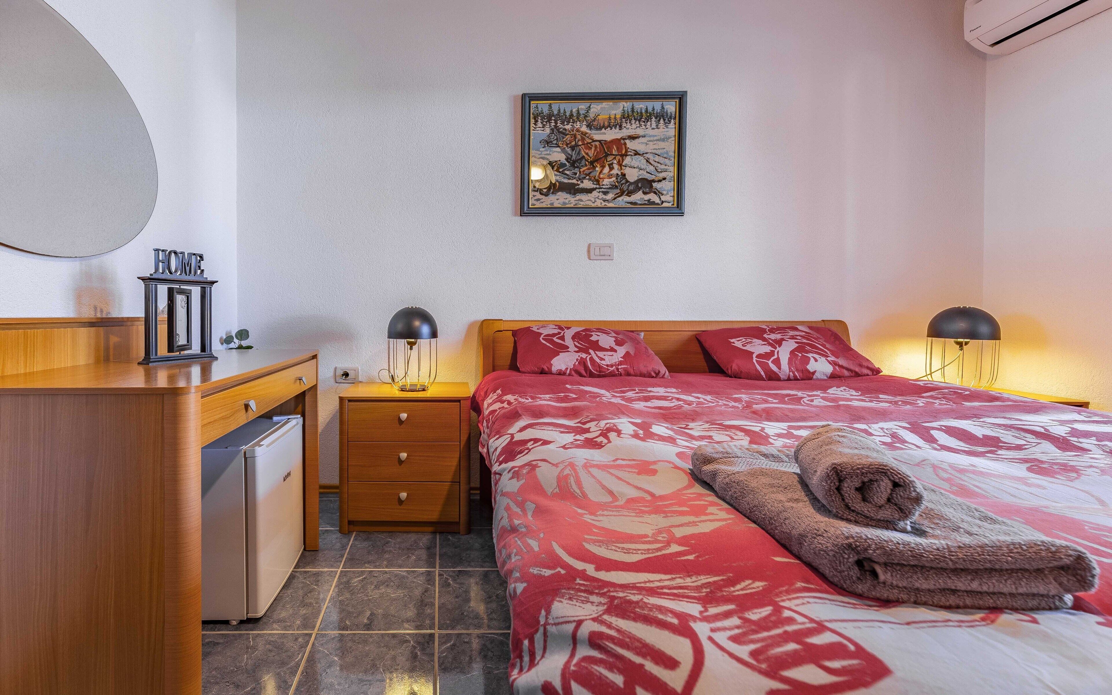 Ein Schlafzimmer mit einem Bett, Nachttischlampen, einem Nachttisch, einer Holzkommode, einem Spiegel und einem Bild an der Wand.