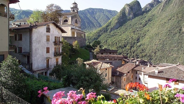 Ein Dorf an einem Hang mit traditioneller Architektur, darunter eine Kirche mit Glockenturm, umgeben von üppiger Vegetation und Bergen im Hintergrund.