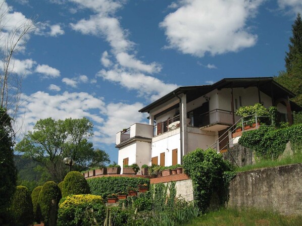A two-story building with a balcony on the upper floor, surrounded by lush greenery and a clear blue sky. - Directly on the lake (Idro)
