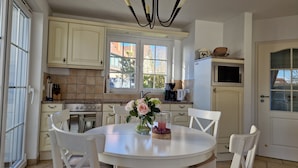 A kitchen with white cabinets, a stove, and a dining table with chairs. - BEAUTIFULLY FURNISHED HOLIDAY HOUSE FOR 4 PEOPLE WITH SEPERATE SAUNA HOUSE (Zingst)