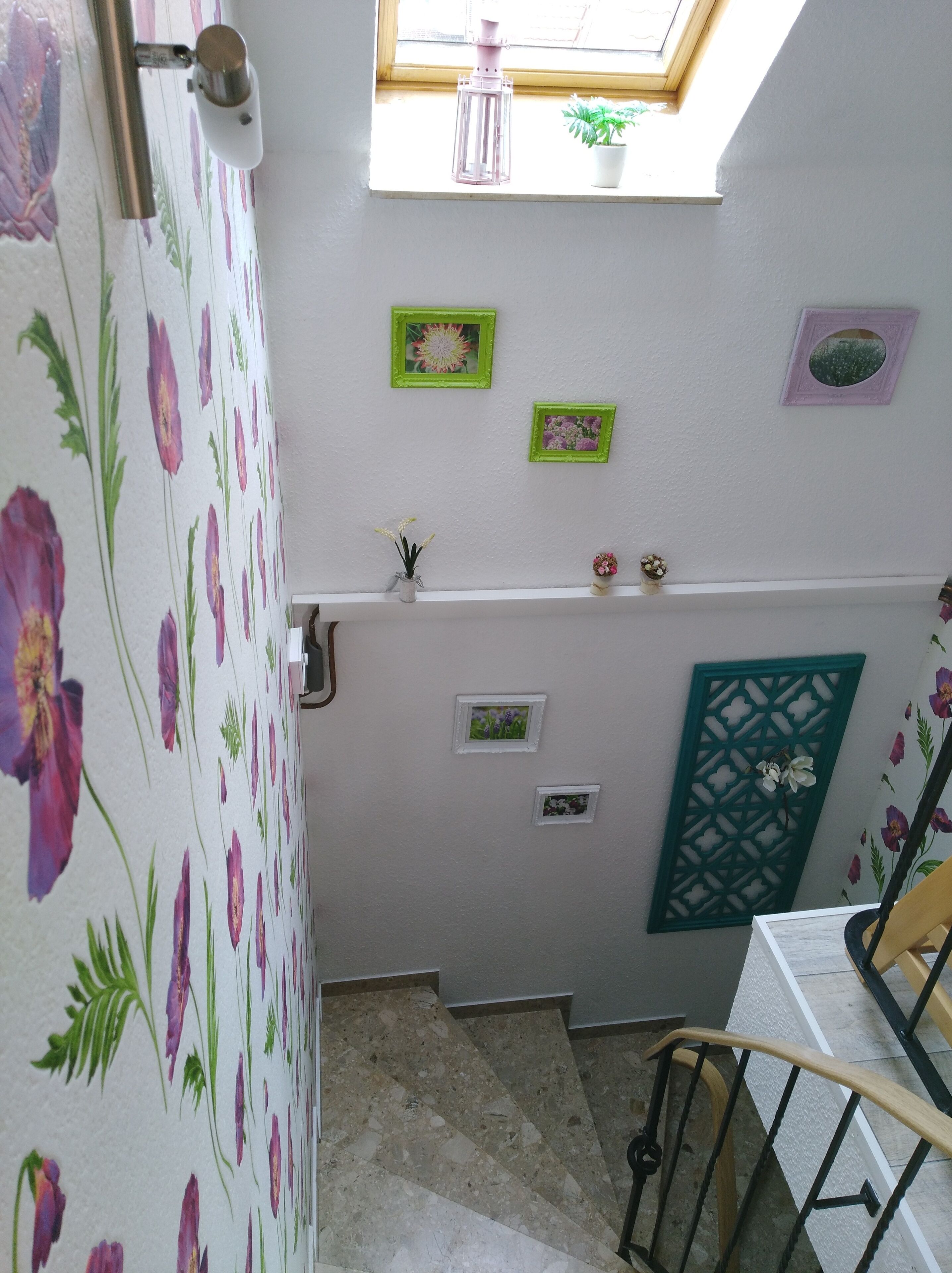 A staircase with floral wallpaper, a skylight, and several framed pictures on the walls.