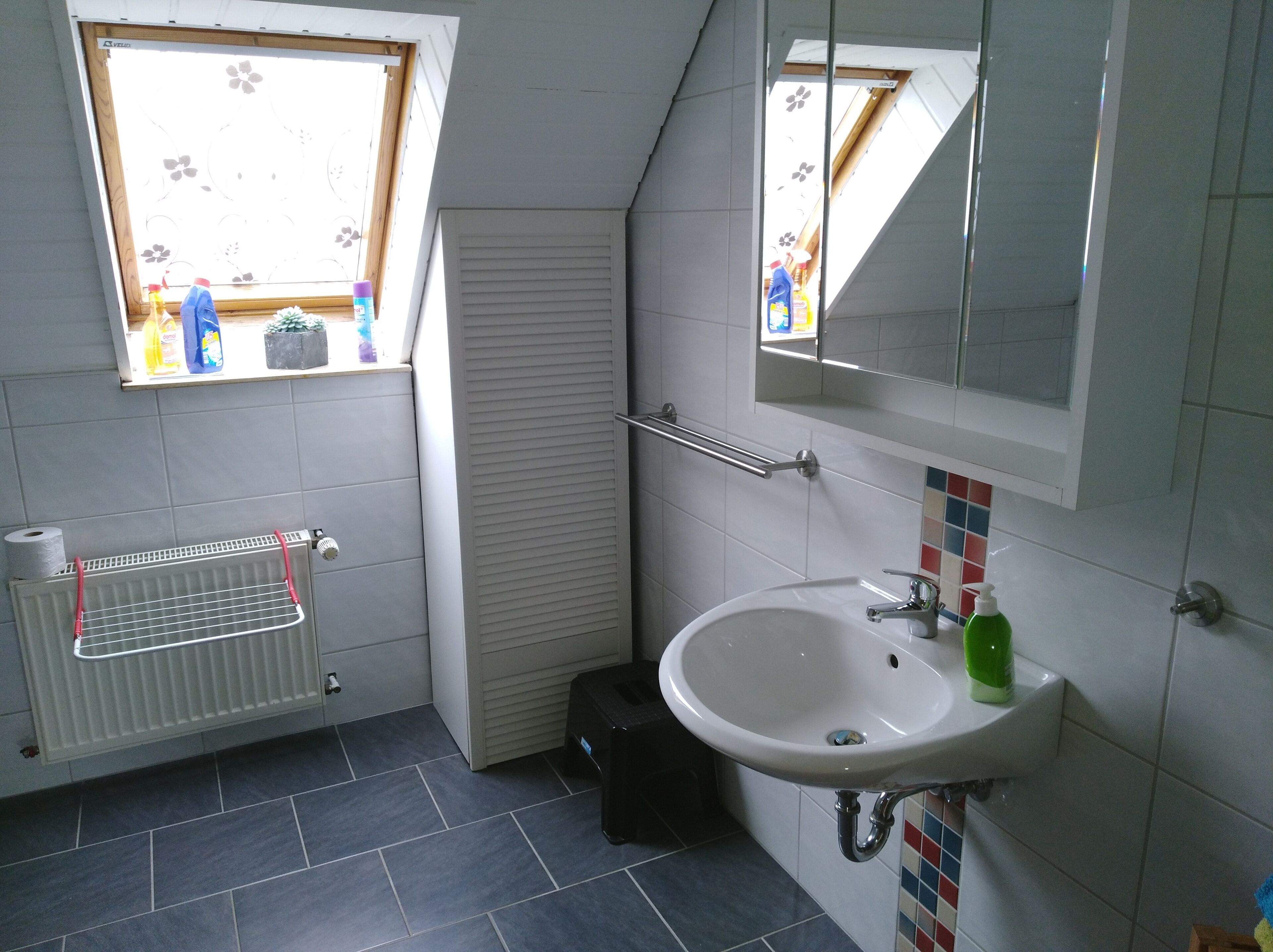 A bathroom with a window, a radiator, a sink, and a mirror.
