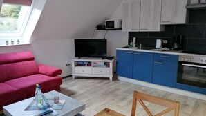 Un espacio habitable compacto con sofá, una mesa de centro, televisor, kitchenette y comedor.