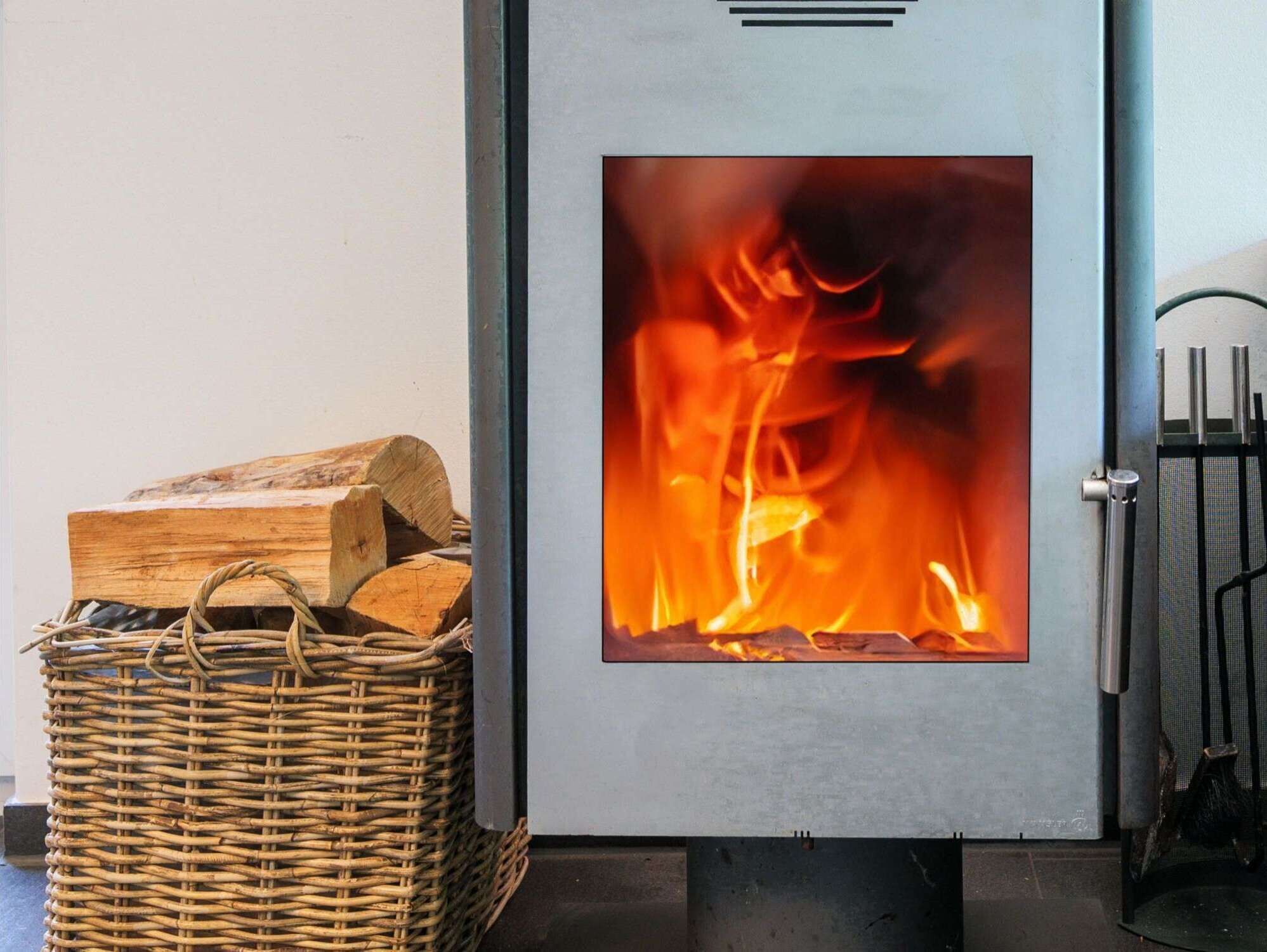 En vedeldad kamin med vedstaplar i en korg bredvid.
