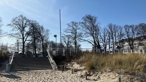 Een zandstrand met een trap die naar een wit gebouw met balkons leidt.
