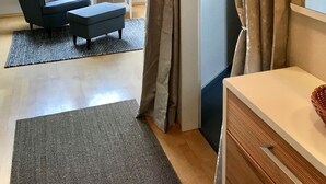 Een kamer met een donkerblauwe fauteuil, een klein wit tafeltje, een lamp en uitzicht door een raam met gordijnen.