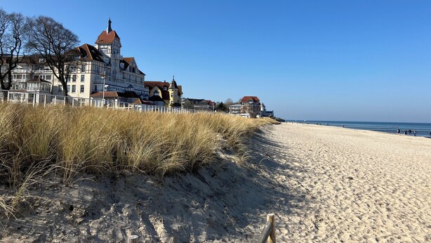 Een gebouw aan de kust met een opvallende toren, gelegen op een zandstrand met een heldere lucht.