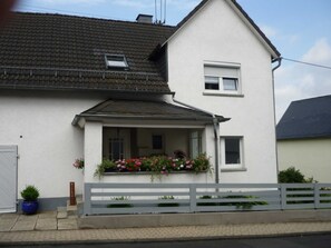 Et toetagers hus med hvide facader, et gråt tag og en lille balkon med blomster.