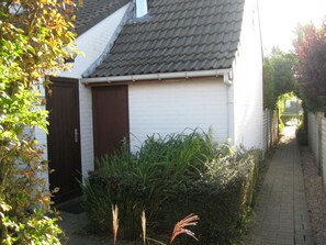 Un petit bâtiment blanc avec une porte marron foncé et un toit recouvert de tuiles.