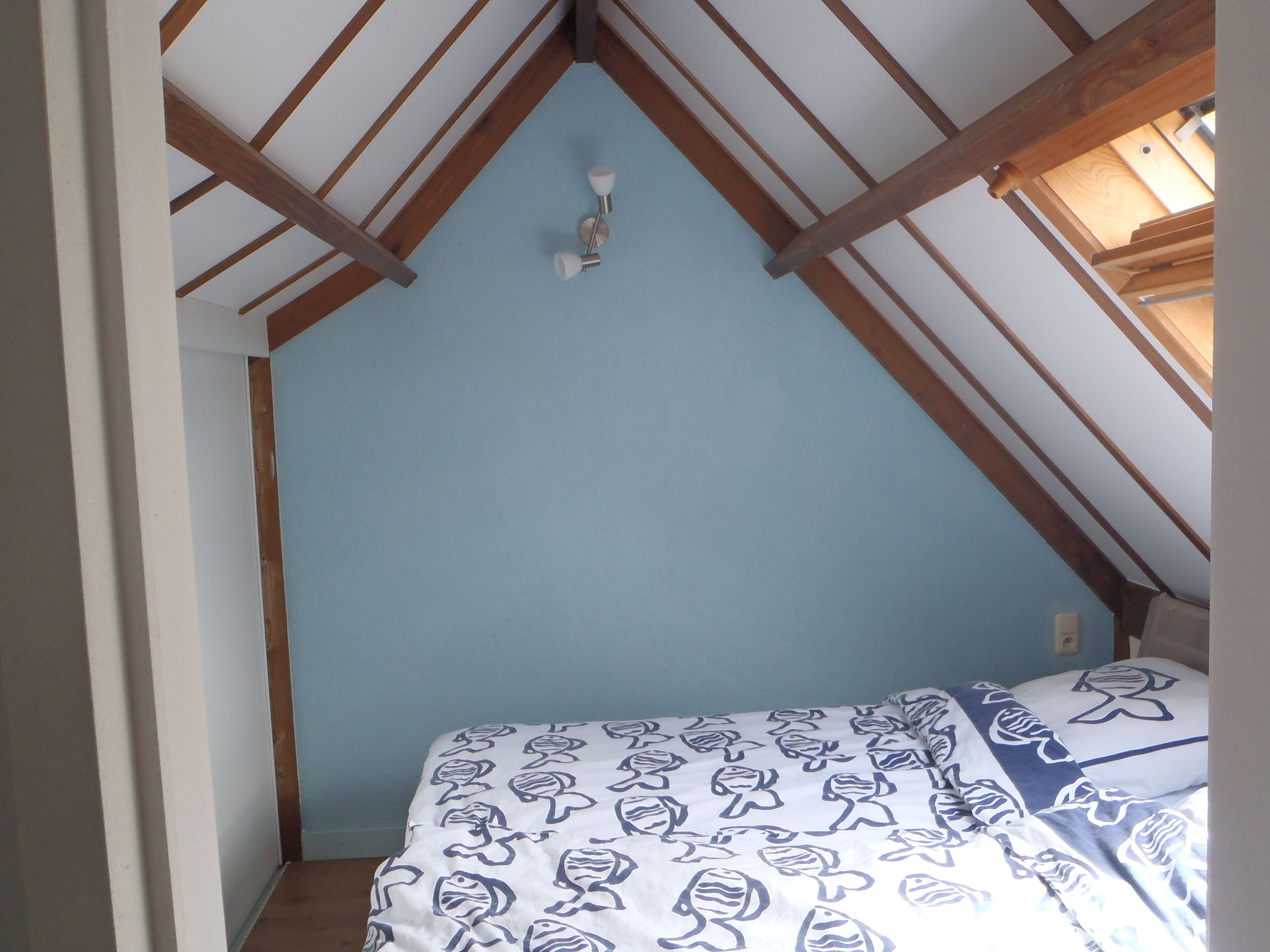 Une chambre avec un plafond en pente, un lit avec une literie à motifs et un luminaire visible.