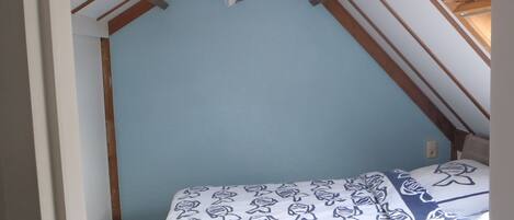 Une chambre avec un plafond en pente, un lit avec une literie à motifs et un luminaire visible.
