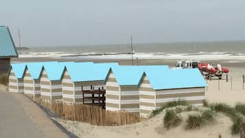 Beach huts line the sandy shore, each with a small entrance and wooden slats.