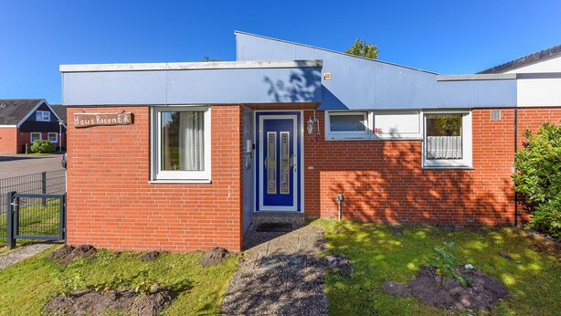 Een gebouw met twee verdiepingen, een blauwe deur en een bord met de tekst 'Haus RosenEdk'.