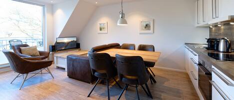 A modern kitchen with a dining area, featuring a wooden table and chairs, a large window, and a view of the outdoors.