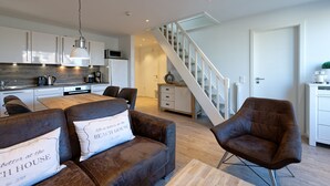 Eine moderne Küche mit weißen Schränken, ein Essbereich mit einem Holztisch und braunen Ledersofas sowie eine Treppe zu einer weiteren Ebene.