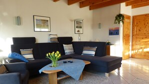 A modern living room with a dark-colored sofa, a coffee table with a vase of yellow flowers, and a wooden floor. - Sunny spacious. DHH, 3 bedrooms, 6 pers., NR, WLan, close to the beach, washer + dryer (Niedersachsen)