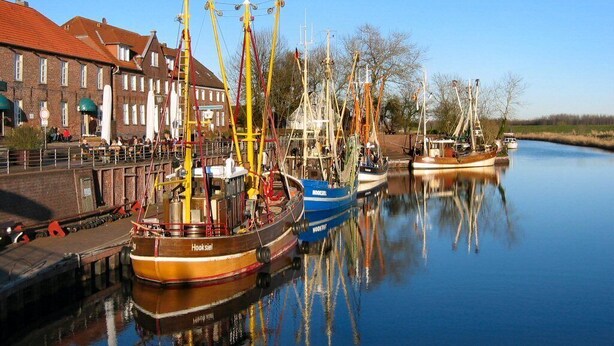 A calm waterway with several boats docked, a bridge, and buildings in the background. - Sunny spacious. DHH, 3 bedrooms, 6 pers., NR, WLan, close to the beach, washer + dryer (Niedersachsen)