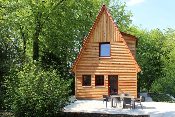 A wooden cabin with a sloped roof, a small window, and a patio with a table and chairs. - Comfortable holiday home with charm, located directly between lake and forest (Möhnesee)