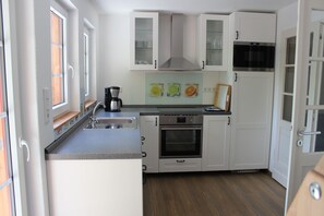 A compact kitchen with white cabinets, a built-in oven, a microwave, and a coffee maker. - Comfortable holiday home with charm, located directly between lake and forest (Möhnesee)