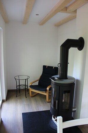 A room with a black wood-burning stove, a wooden chair, a small glass table, and a white bench. - Comfortable holiday home with charm, located directly between lake and forest (Möhnesee)