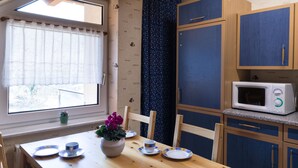 Une cuisine compacte avec une table en bois pour quatre personnes, un four à micro-ondes et des placards aux couleurs bleu et beige.