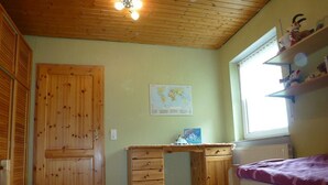 Une pièce avec un bureau en bois, un lit, une carte accrochée au mur et une fenêtre.