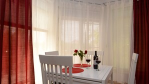 Un coin repas avec une table blanche, des sets de table rouges et un vase rempli de fleurs rouges.
